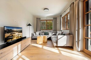 A modern living room with a large flat-screen TV, a sofa set, a coffee table, and a floor lamp. - Garden Suite by Alpine Host Helpers (Kirchberg in Tirol)