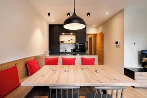 A modern dining area with a wooden table, red cushions, and a black pendant light. - Garden Suite by Alpine Host Helpers (Kirchberg in Tirol)