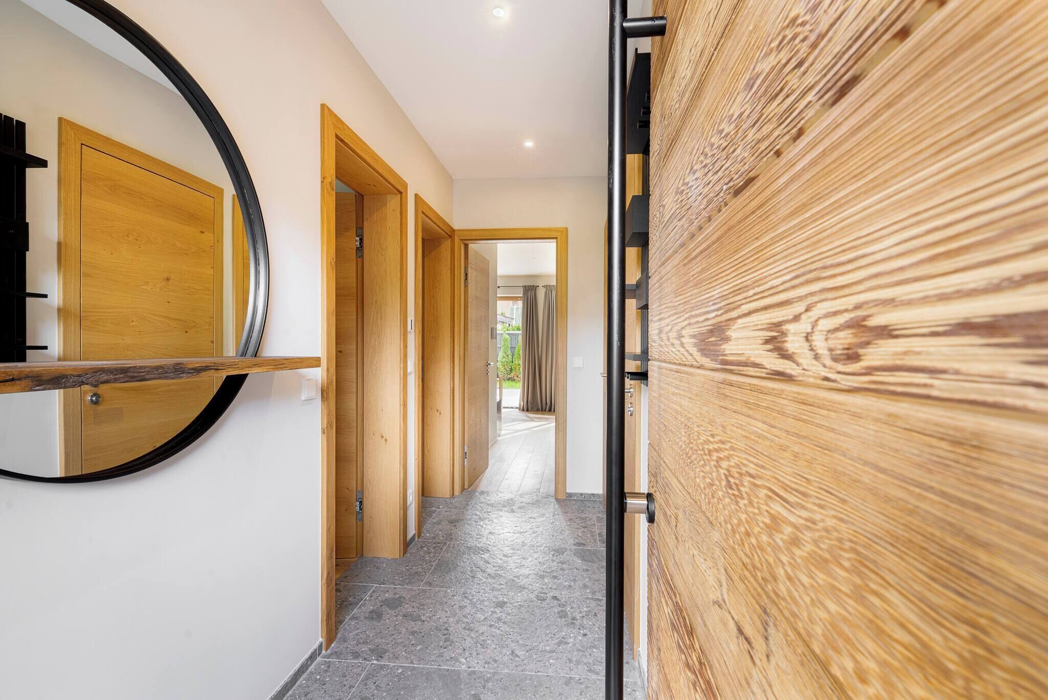 Un pasillo con una puerta de madera, un espejo y vista a otra habitación.