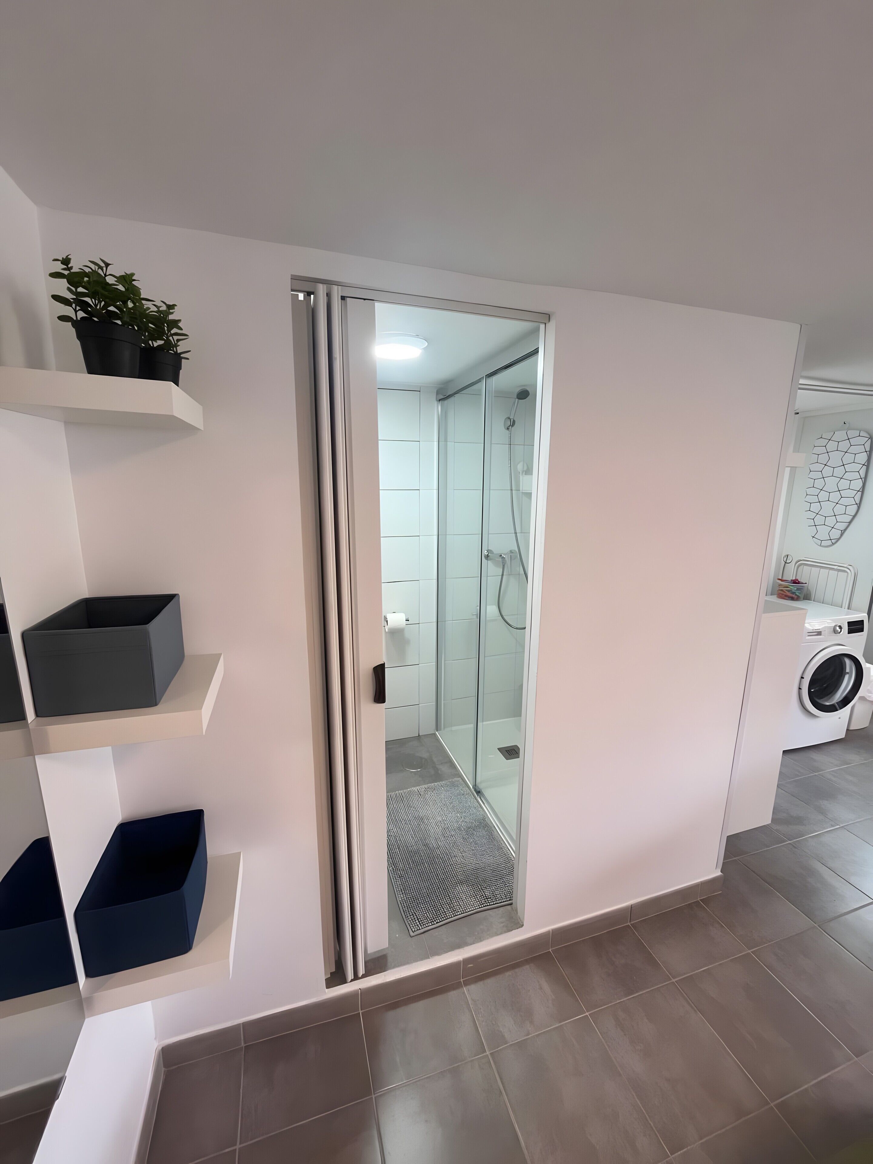 Un baño moderno con cabina de ducha de vidrio, lavadora integrada y estantes de almacenamiento.