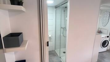Un baño moderno con cabina de ducha de vidrio, lavadora integrada y estantes de almacenamiento.