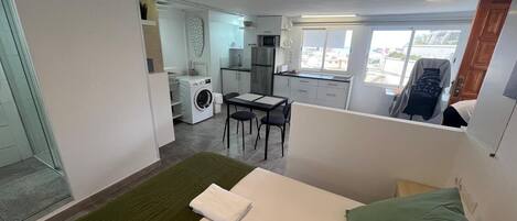 A hotel room with a bed, a small table, a chair, a washing machine, and a kitchenette.