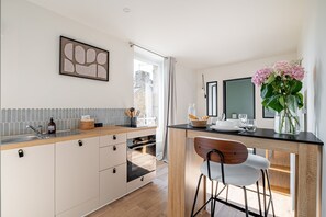 A modern kitchen with a central island, a dining area with a chair, and a view of the outside. - Le Carré des Skippers - Sur les quais du port (La Trinite-sur-Mer)