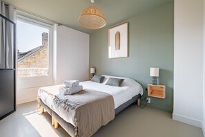 Ein modernes Schlafzimmer mit einem großen Bett, Nachttischlampen und Blick auf ein Steinhaus durch das Fenster.