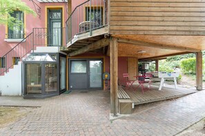 A two-story building with a wooden deck, a covered outdoor seating area, and a glass door entrance. - Le Cottage - Studio avec véranda et jardin (Lyon)