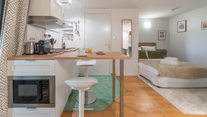 Kompakti hotellihuone, jossa on pieni keittiönurkkaus, vihreä tyyny ja pieni kylpyhuone.