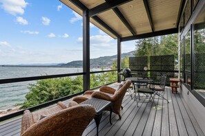 A covered outdoor deck with wicker furniture and a view of the water. - Luxury Lakefront Retreat | Private Beach Near Town (Sagle)