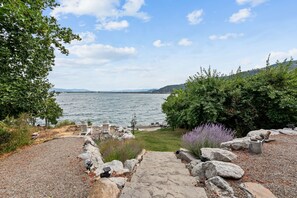 A stone pathway leading to a lakeside view with a chair and a birdcage. - Luxury Lakefront Retreat | Private Beach Near Town (Sagle)