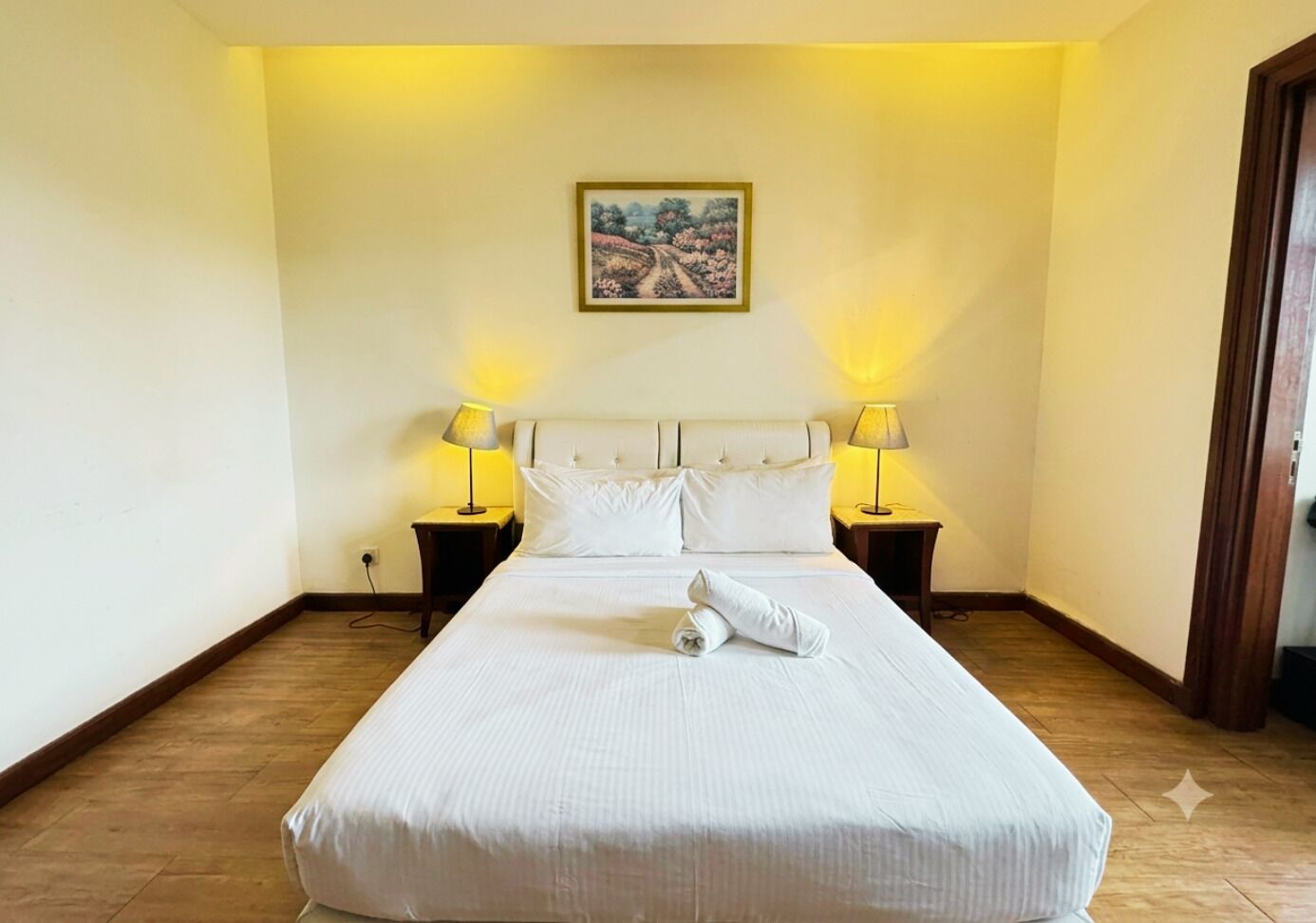 Habitación de hotel con una cama grande, dos lámparas de noche, un cuadro en la pared y suelo de madera.