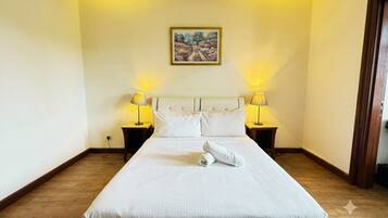 Habitación de hotel con una cama grande, dos lámparas de noche, un cuadro en la pared y suelo de madera.