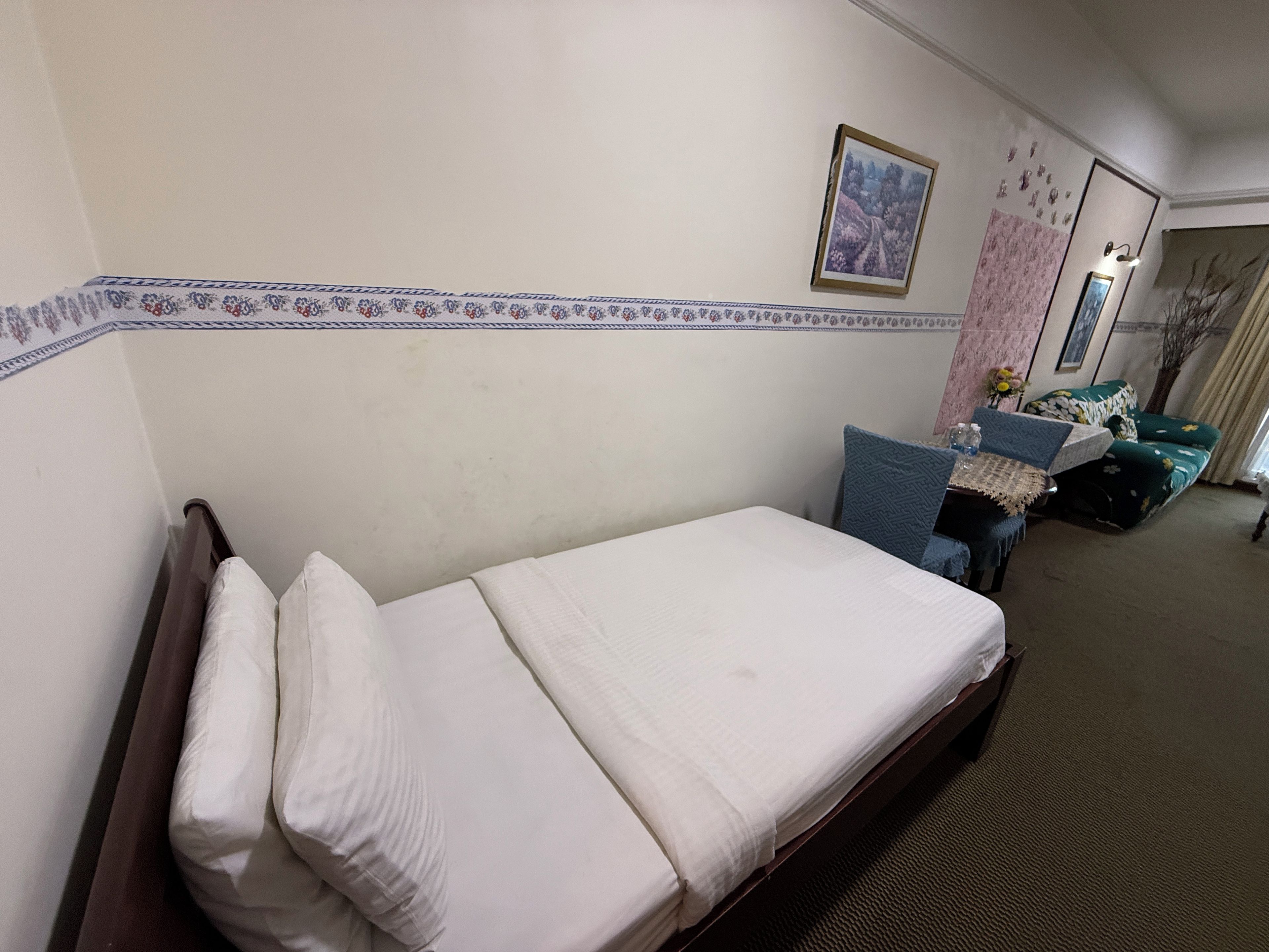 A hotel room with a single bed, a small table with a chair, a sofa, and a wall-mounted picture.