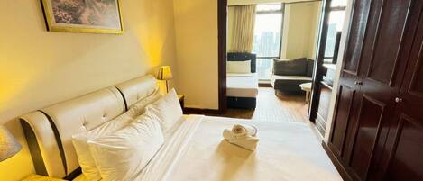 A hotel room with a bed, a nightstand, a lamp, a painting on the wall, and a view of the city through the window.
