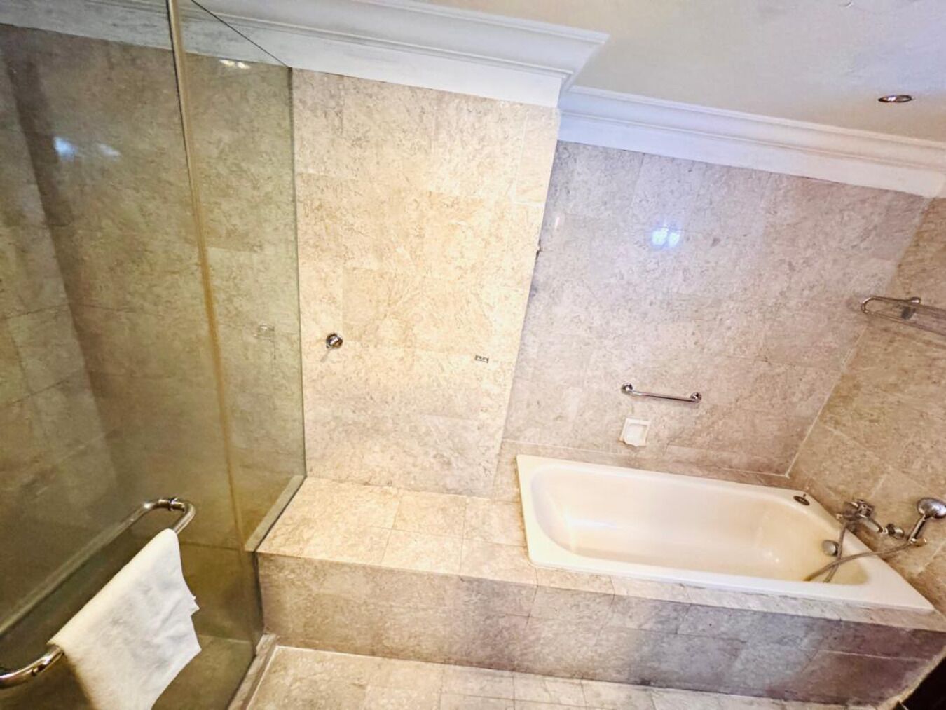 A bathroom with a glass-enclosed shower, a marble-tiled wall, and a freestanding bathtub.
