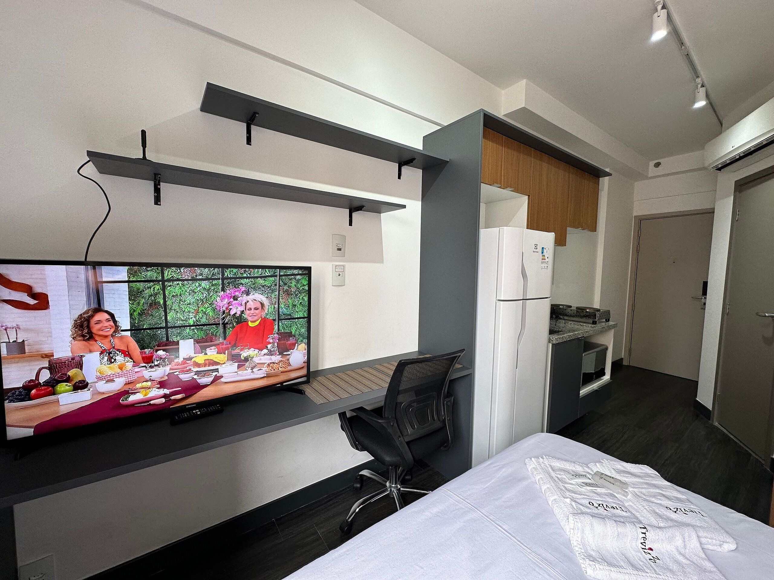 Una habitación de hotel moderna con televisión de pantalla plana, una cama, un escritorio y una kitchenette.