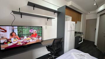 Una habitación de hotel moderna con televisión de pantalla plana, una cama, un escritorio y una kitchenette.