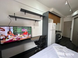 Quarto de hotel moderno com televisão de ecrã plano, uma cama, uma secretária e uma kitchenette.