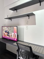 Un televisor montado en la pared, con un escritorio y una silla debajo.