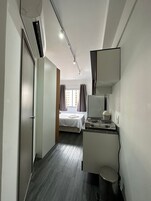 Habitación de hotel con cama, kitchenette pequeña, espejo y ventana con cortinas.