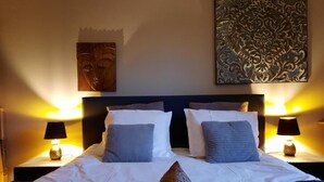 Een bed met witte lakens, twee kussens, een geweven mat en twee bedlampjes.