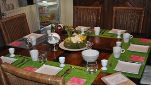 Een eettafel gedekt voor vier personen, met een groene placemat, wit servies en een middelpunt.