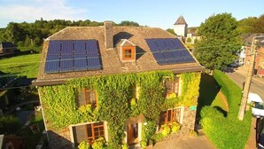 Een gebouw met zonnepanelen op het dak, muren begroeid met klimop en een klein raam.