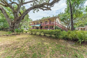 A two-story building with a balcony, surrounded by trees and a grassy area.