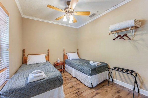 A bedroom with two beds, a ceiling fan, a wall-mounted towel rack, and a wooden floor.
