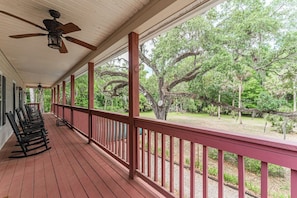 A covered porch with a ceiling fan, wooden rocking chairs, and a view of a wooded area.