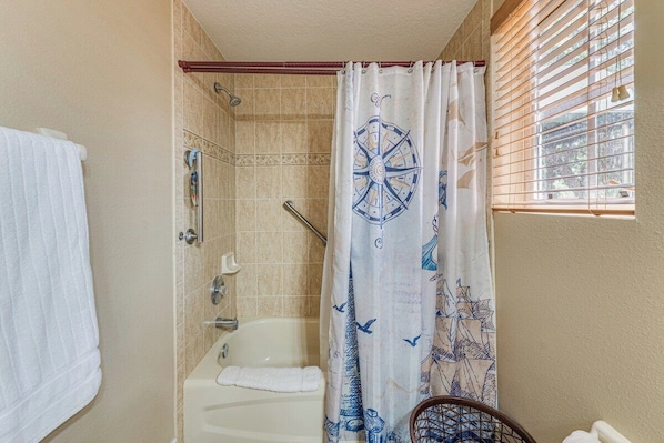 A bathroom with a bathtub, a shower, and a window with blinds.
