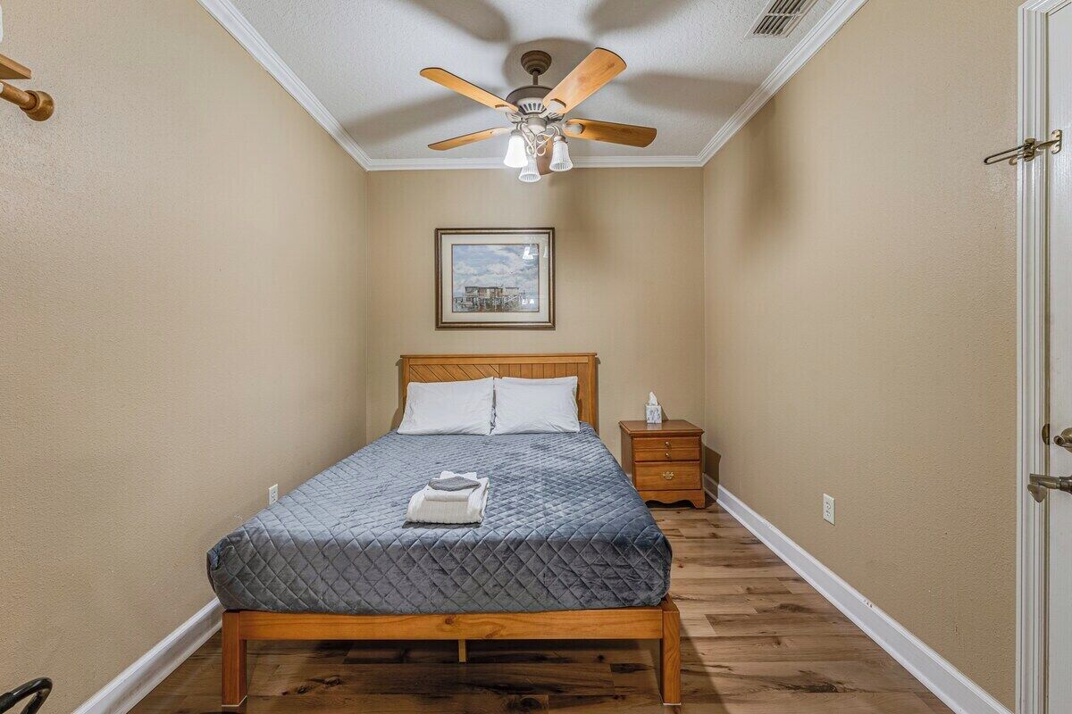 A bedroom with a bed, a nightstand, a ceiling fan, and a framed picture on the wall.