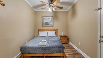A bedroom with a bed, a nightstand, a ceiling fan, and a framed picture on the wall.