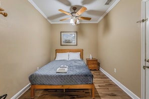 Une chambre à coucher avec un lit, une table de chevet, un ventilateur de plafond et un tableau encadré au mur.