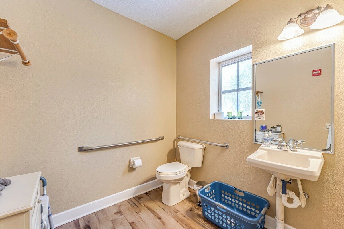 A bathroom with a toilet, sink, and handrails.