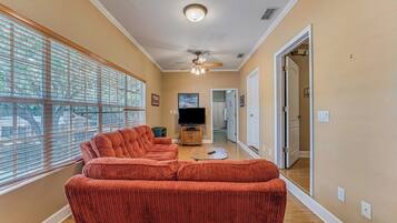 A living room with a large window, a ceiling fan, and a television.