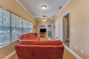 A living room with a large window, a ceiling fan, and a television.