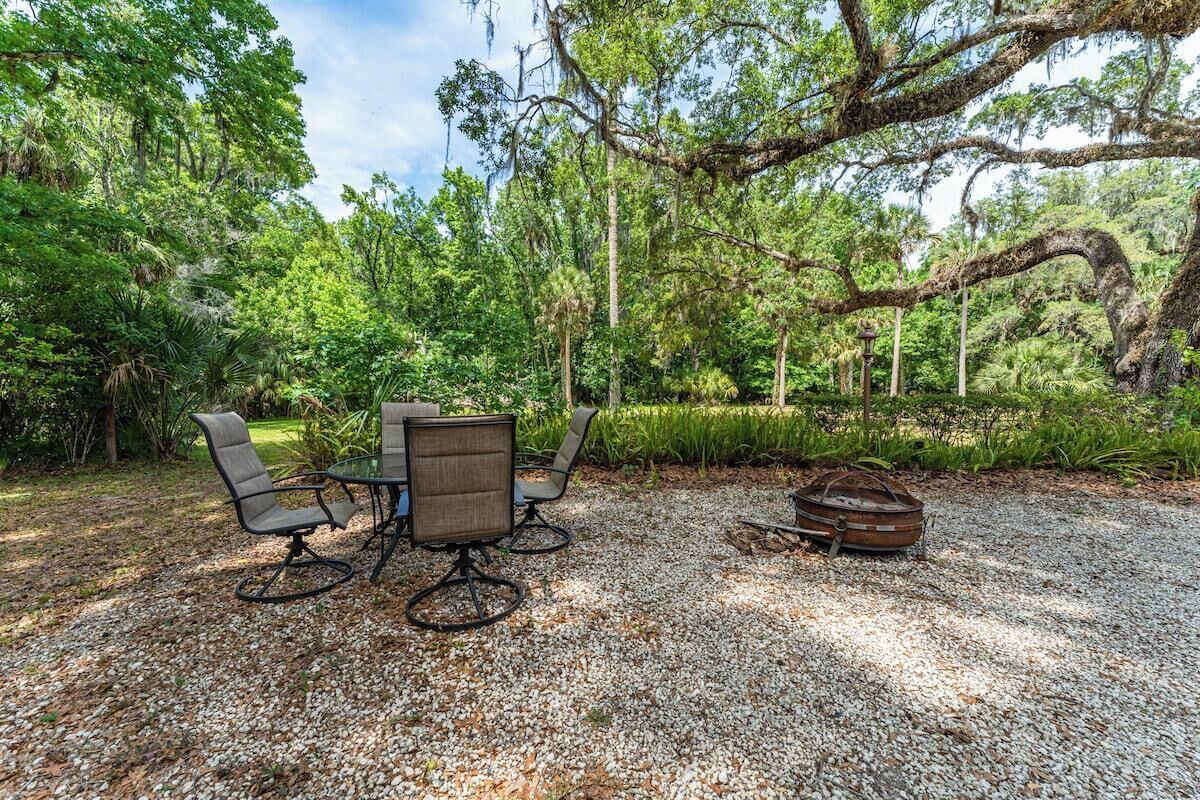 An outdoor seating area with a table and chairs, surrounded by trees and a gravel ground.