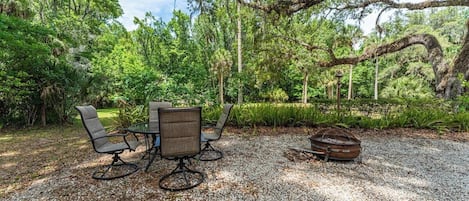 An outdoor seating area with a table and chairs, surrounded by trees and a gravel ground.