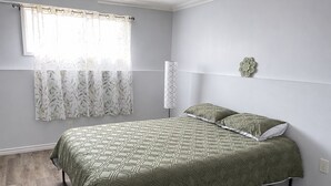 Une chambre à coucher avec un lit, une fenêtre avec un rideau, une lampe fixée au mur et un élément décoratif mural.