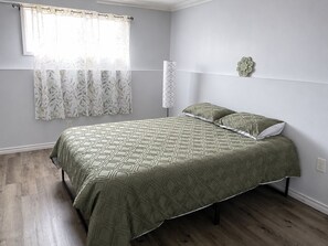 A bedroom with a bed, a window with a curtain, a wall-mounted lamp, and a decorative wall piece. - Spacious home, 10 min to wineries and many attractions. Free parking & wifi (Welland)