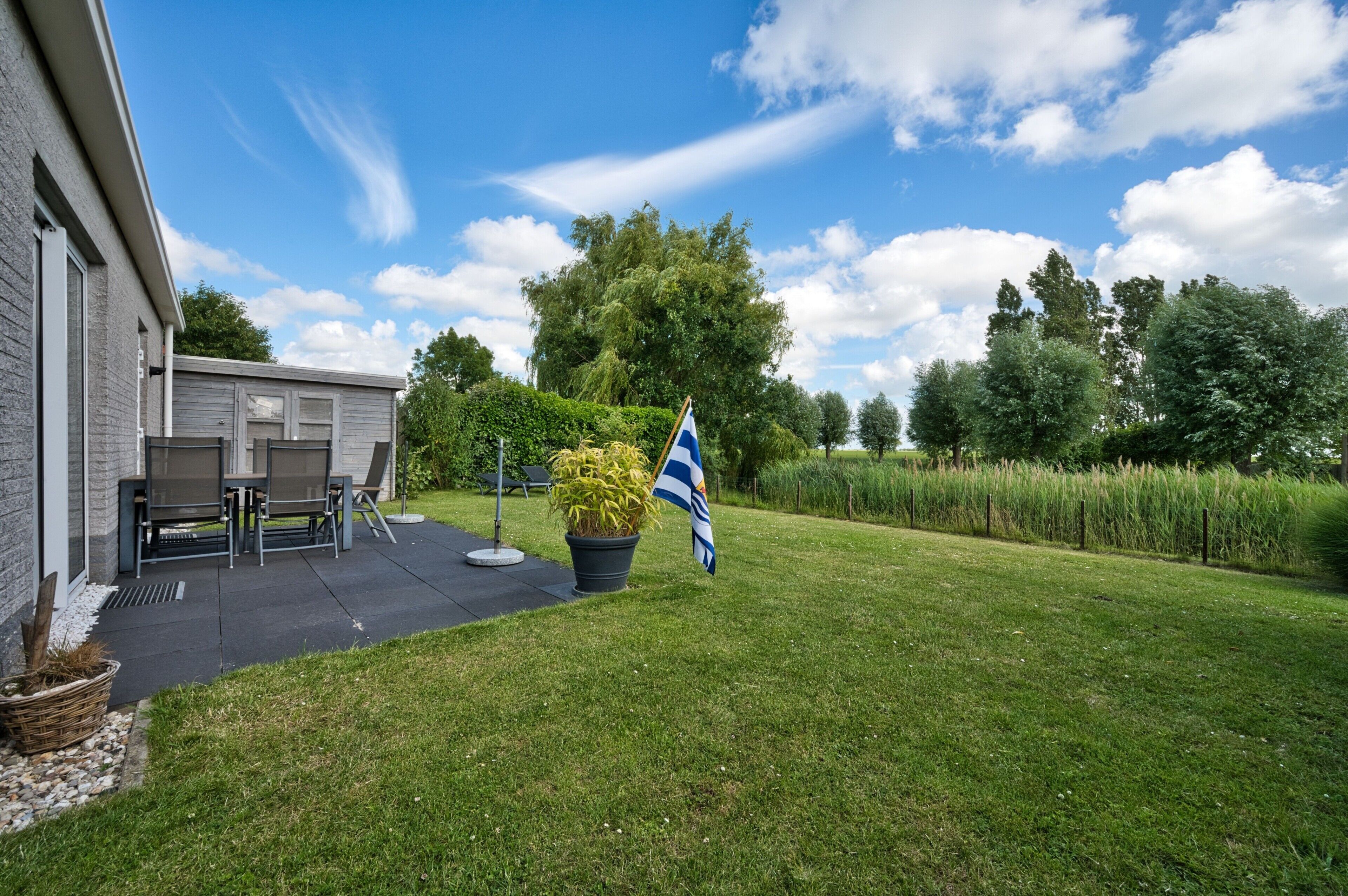 A residential property with a patio, outdoor furniture, a flag, and a well-maintained lawn.