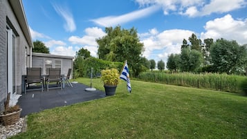 A residential property with a patio, outdoor furniture, a flag, and a well-maintained lawn.