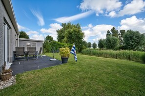 Ein Wohnhaus mit Terrasse, Gartenmöbeln, einer Flagge und einem gepflegten Rasen.