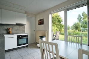 A modern kitchen with a built-in oven, a dining table with chairs, and a sliding glass door leading to a garden.
