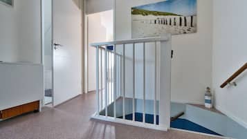 Een hal met een witte trapleuning, een schilderij van een strandtafereel, en een klein speelgoedvuurtoren.