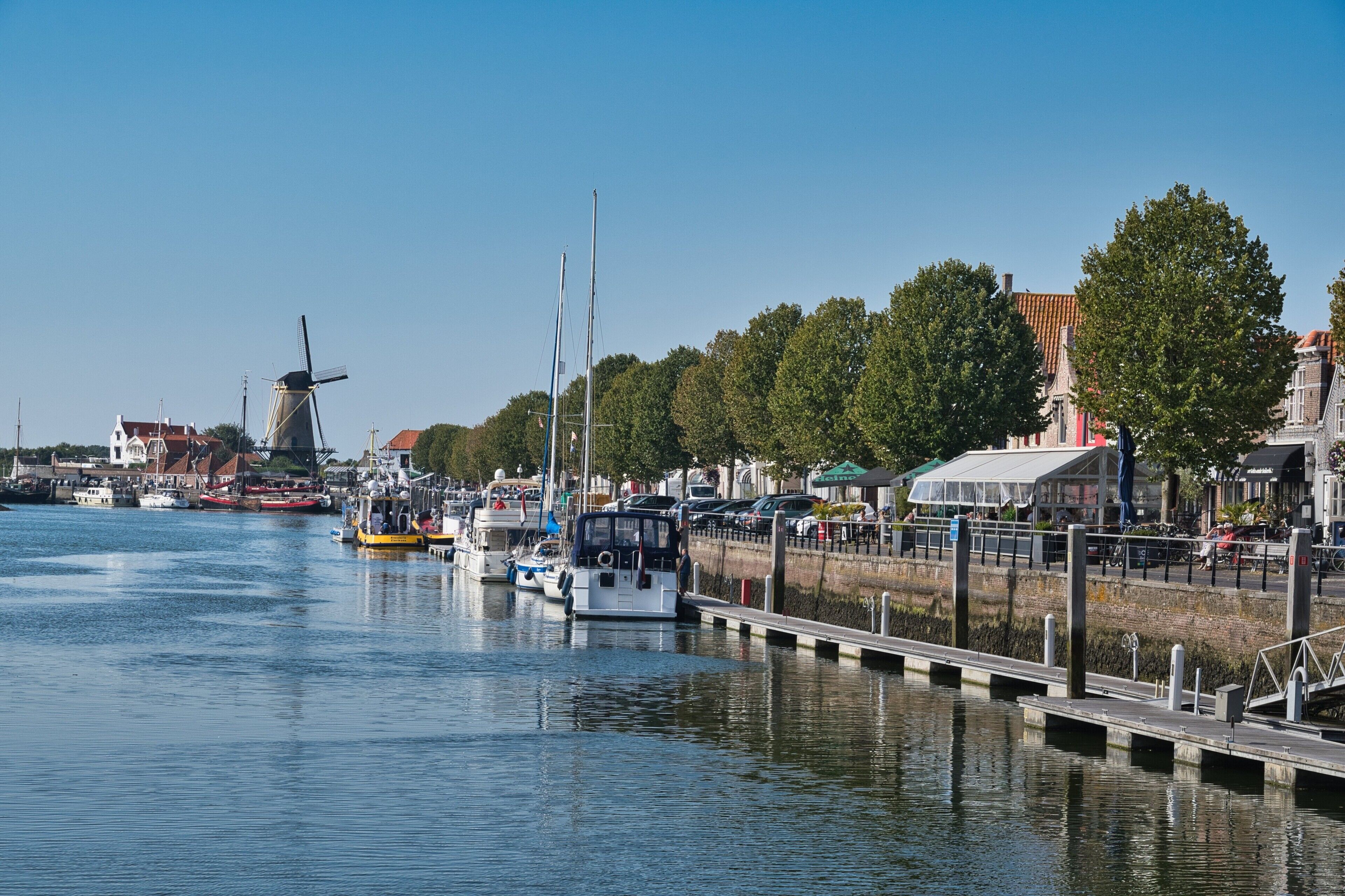 A harbor with boats docked, a windmill, and buildings along the waterfront.