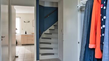 A hallway with a tiled floor, a staircase, and a clothing rack with various garments.