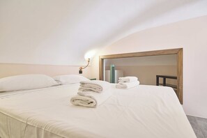Ein Hotelzimmer mit einem ordentlich bezogenen Bett, einem großen Spiegel und einem Nachttisch mit einer Lampe.