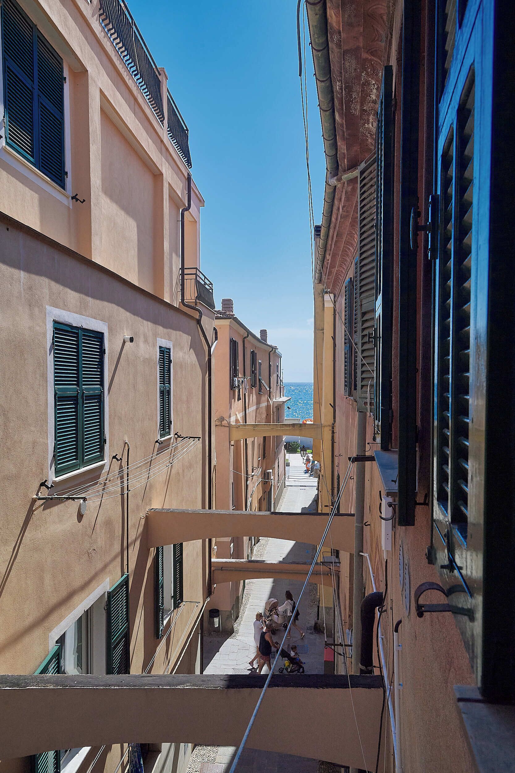 A narrow street with buildings on either side, featuring balconies and shutters.