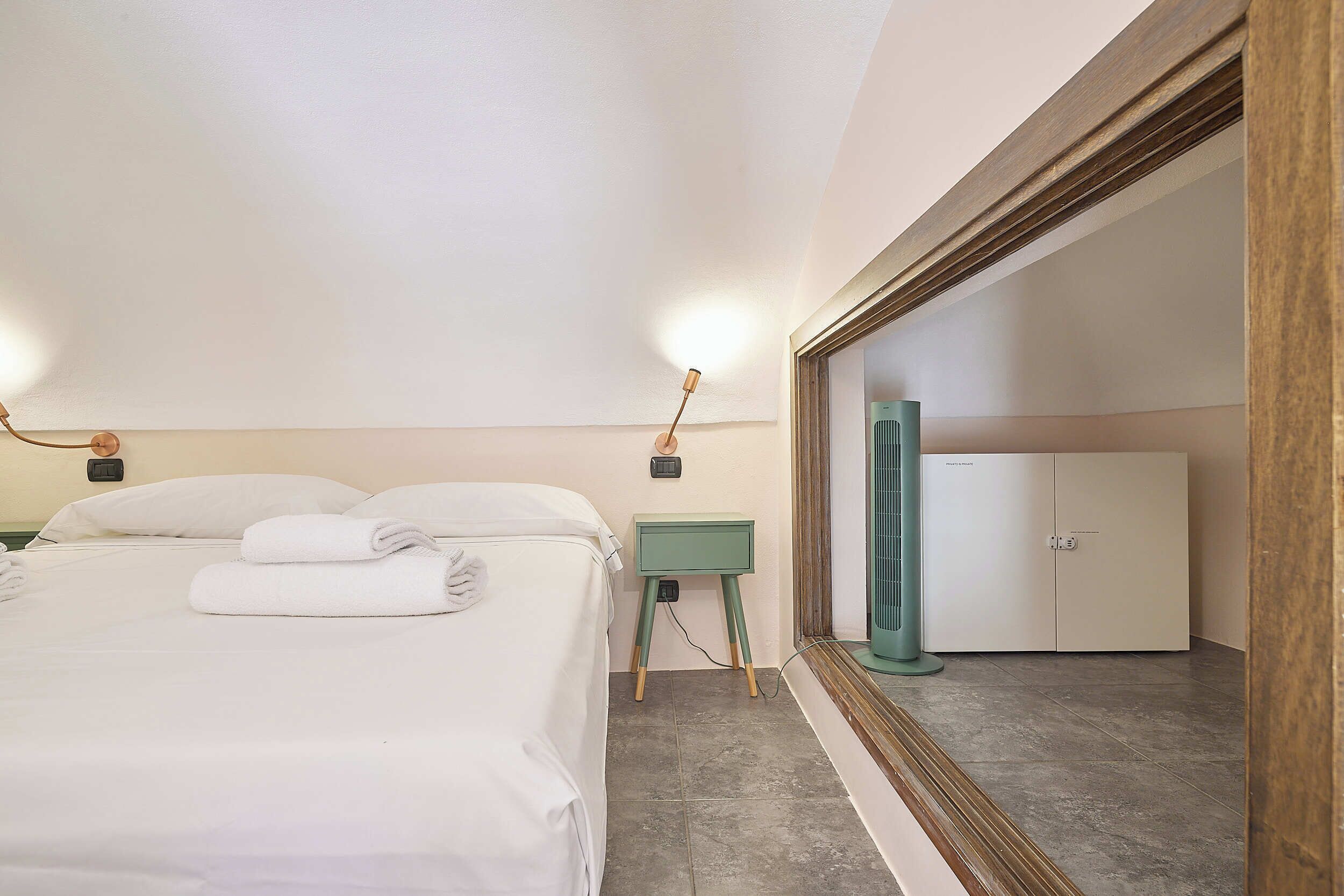 A hotel room with a bed, a nightstand, a mirror, and a wardrobe.