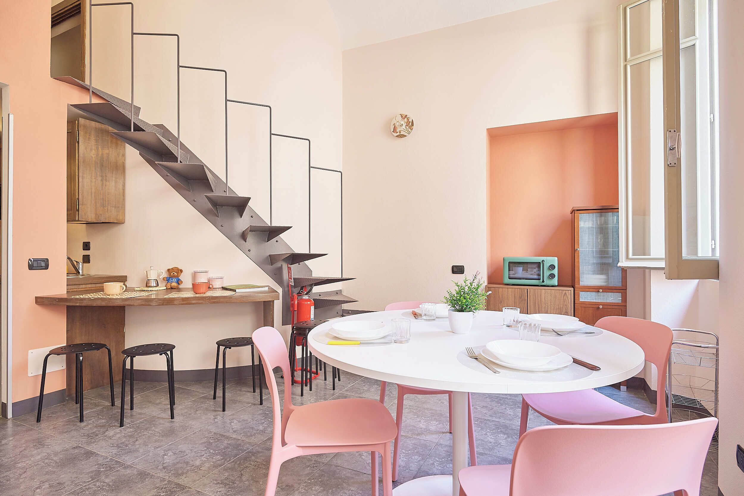 Eine moderne Küche mit Treppe, Essbereich mit rosa Stühlen und einem kleinen Tisch für zwei Personen.